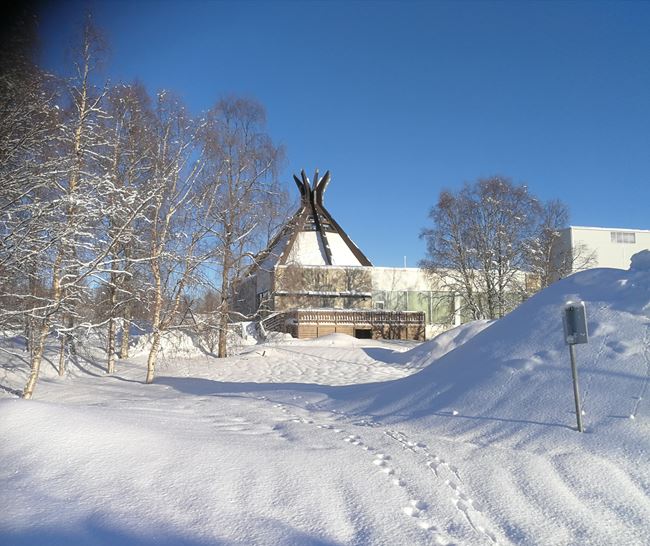 Talvinen ja luminen maisema, jossa taustalla näkyy kotamainen rakennus